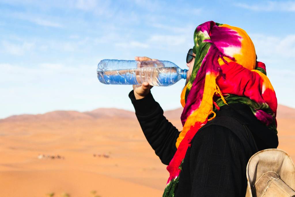 Person hydrating with water bottle during lunch in scorching desert sun
